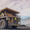 Large mining dump truck and bulldozer operating at an open-pit mine with mountains in the background.